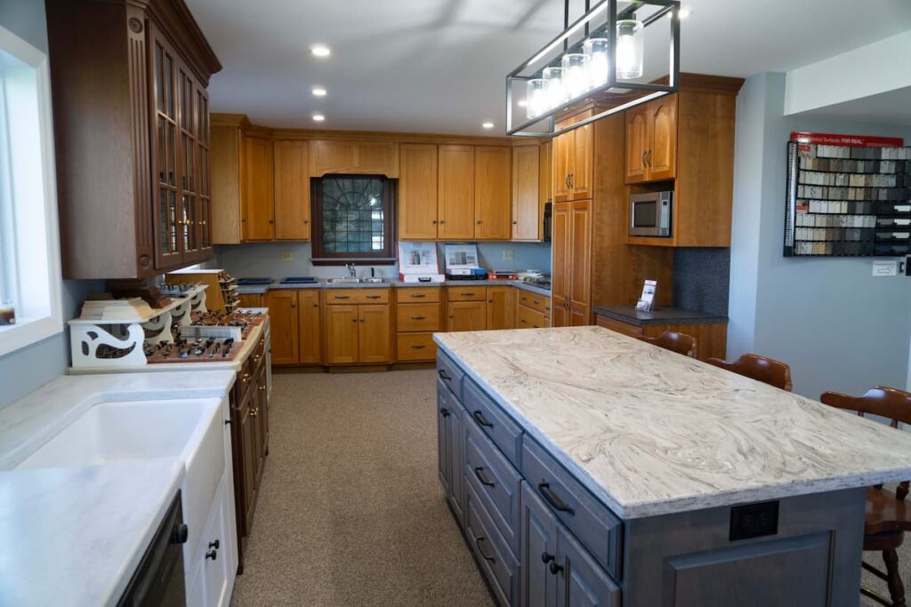 Display kitchen in the Rissler Custom Kitchens showroom, with oak and cherry cabinetry around a gray island topped with a marbled countertop.