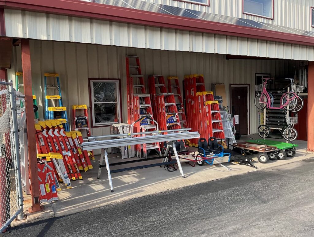 Fiberglass and aluminum ladders, carts, and bicycles displayed under the front awning at Shady Lane Hardware.