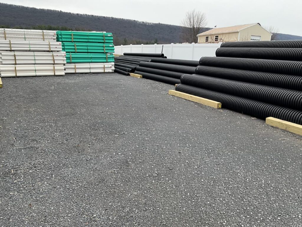Outdoor storage yard at Shady Lane Hardware stacked with PVC pipe and black corrugated drainage pipe.