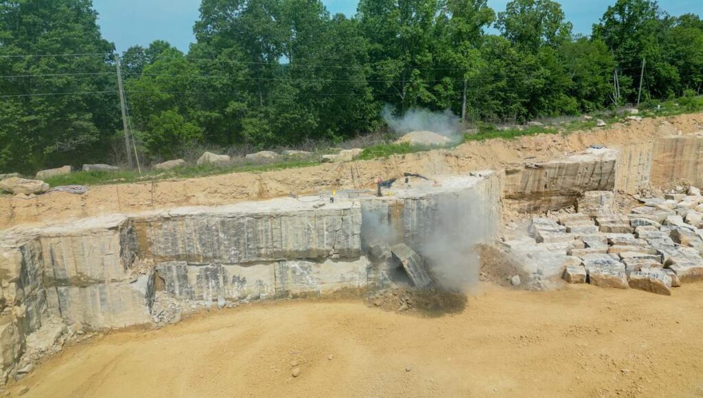 Dust and debris burst from a sandstone quarry wall as a blast breaks loose a large section of stone.