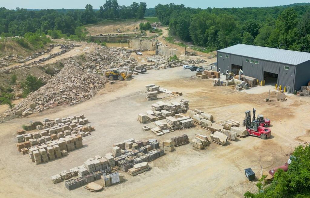 Aerial view of Briar Hill Sandstone's yard, with pallets of cut sandstone, a red forklift, the metal mill building, and the working quarry behind it.