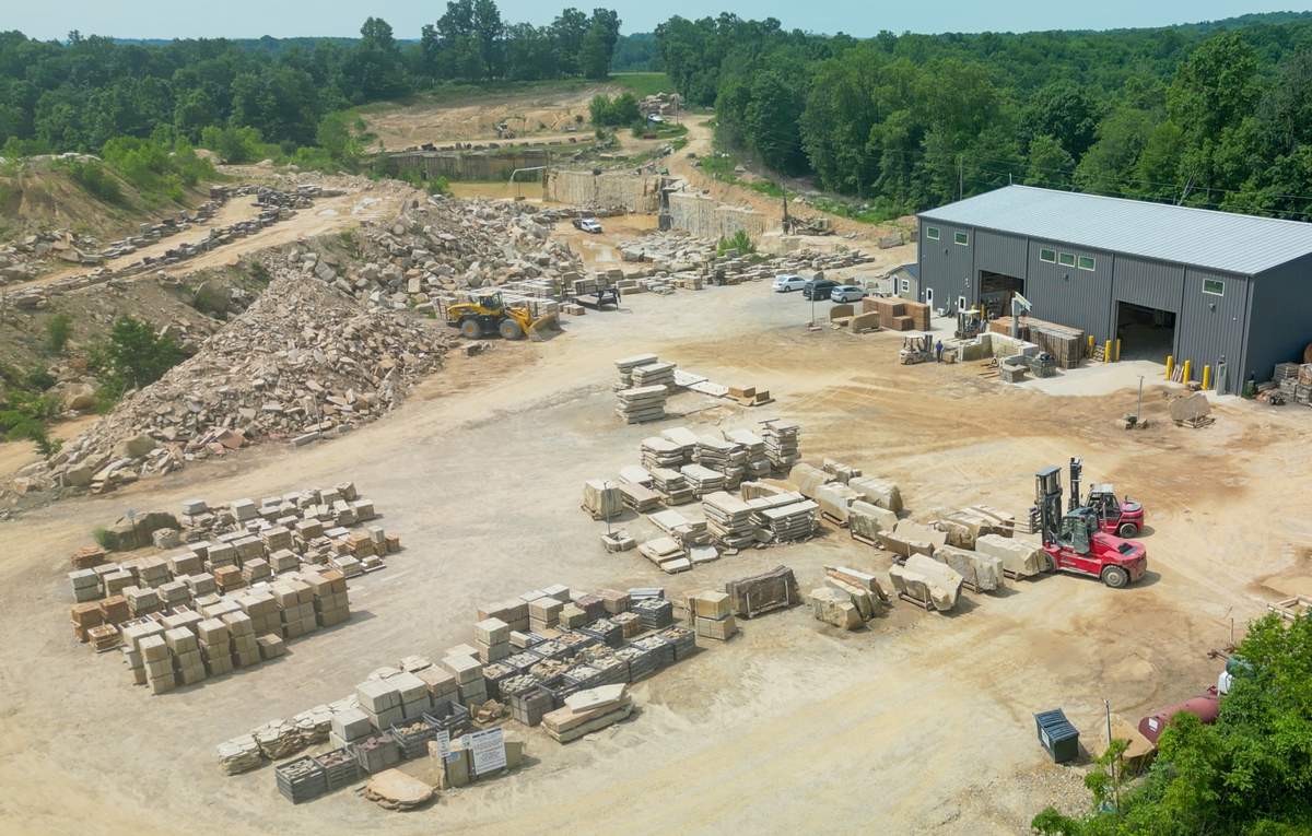 Aerial view of Briar Hill Sandstone's yard, with pallets of cut sandstone, a red forklift, the metal mill building, and the working quarry behind it.