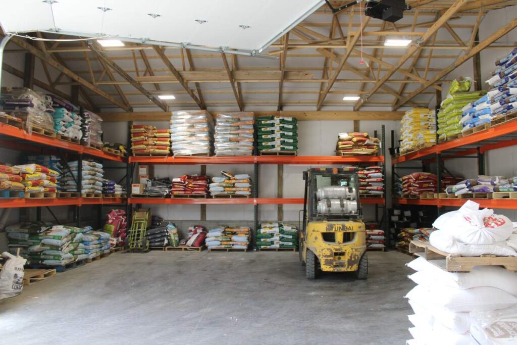 A forklift sits between orange racks stacked with bagged feed in Maysville Elevator's ground-level warehouse.